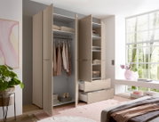 Moderner beigefarbener Kleiderschrank mit geöffneten Türen, Kleiderstange, Regalböden und zwei ausgezogenen Schubladen im hellen Schlafzimmer; Ansicht schräg von vorn.