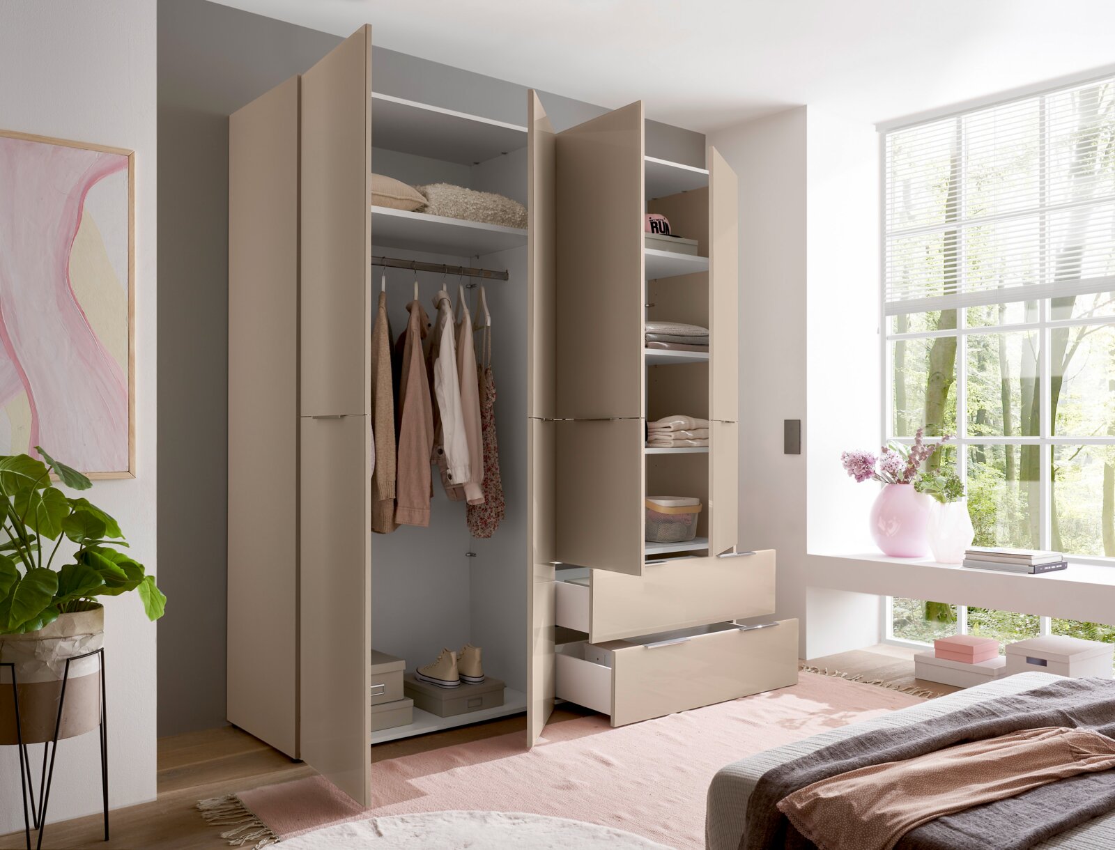 Moderner beigefarbener Kleiderschrank mit geöffneten Türen, Kleiderstange, Regalböden und zwei ausgezogenen Schubladen im hellen Schlafzimmer; Ansicht schräg von vorn.
