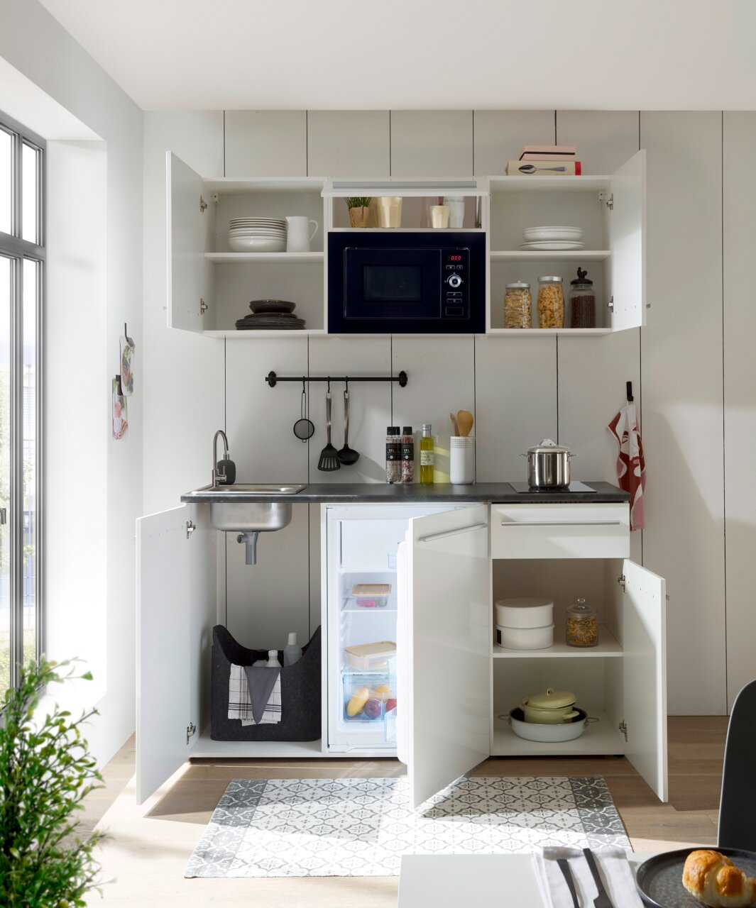 Moderne Single-Küche mit offenem Schrank, Mikrowelle, Spüle und Kühlschrank, aus der Frontalperspektive fotografiert.