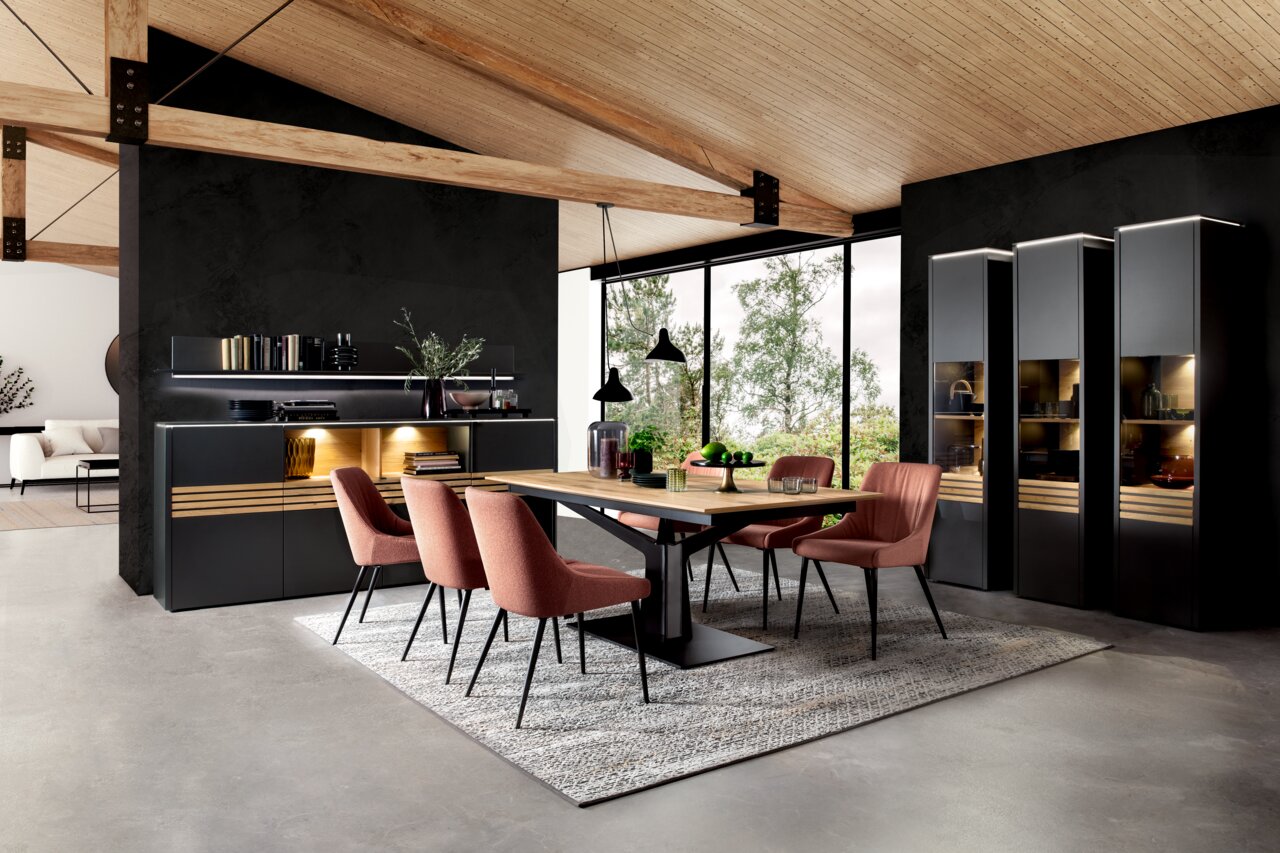 Moderne Esszimmer-Einrichtung mit Highboard, Vitrine und Esstisch in einem offenen Raum mit Holzdecke und großen Fenstern, seitliche Perspektive.