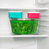 Grüne Salatschleuder Easy Spin im Kühlschrank, seitliche Perspektive, mit zwei bunten Vorratsdosen obenauf.