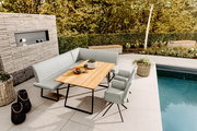 Modernes Outdoor-Ess-Set auf einer Poolterrasse: hellgraue gepolsterte Eckbank mit zwei passenden Stühlen und rechteckigem Holztisch mit schwarzem Metallgestell, fotografiert in schräger Perspektive von vorne oben.