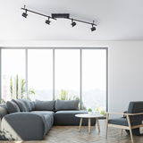 Moderne schwarze Wand- und Deckenleuchte mit vier verstellbaren Strahlern, montiert an einer Wohnzimmerdecke, seitliche Perspektive.