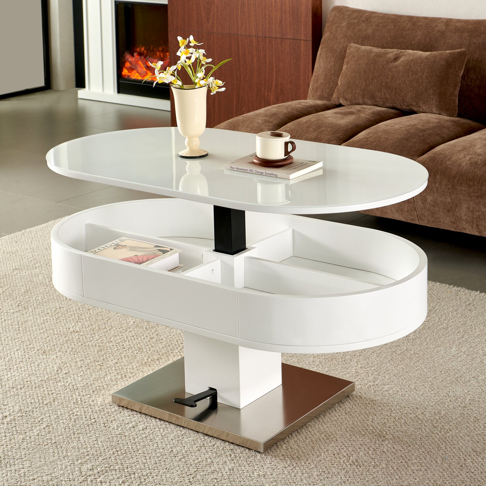 Weißer, höhenverstellbarer Couchtisch mit ovaler Tischplatte und Ablagefach auf Metallfuß im Wohnzimmer neben braunem Sofa, perspektivisch in schräger Frontansicht von leicht oben.