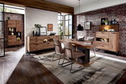 Moderne Esszimmer-Einrichtung mit Holzmöbeln, bestehend aus einem Esstisch, Sideboard und Vitrine, in einem Raum mit Backsteinwand und großen Fenstern. Perspektive von vorne.