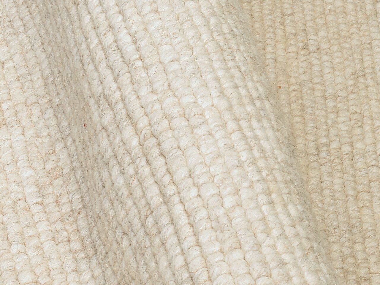 Nahaufnahme eines handgewebten Teppichs in cremeweißer Farbe mit strukturierter Oberfläche, seitliche Perspektive.