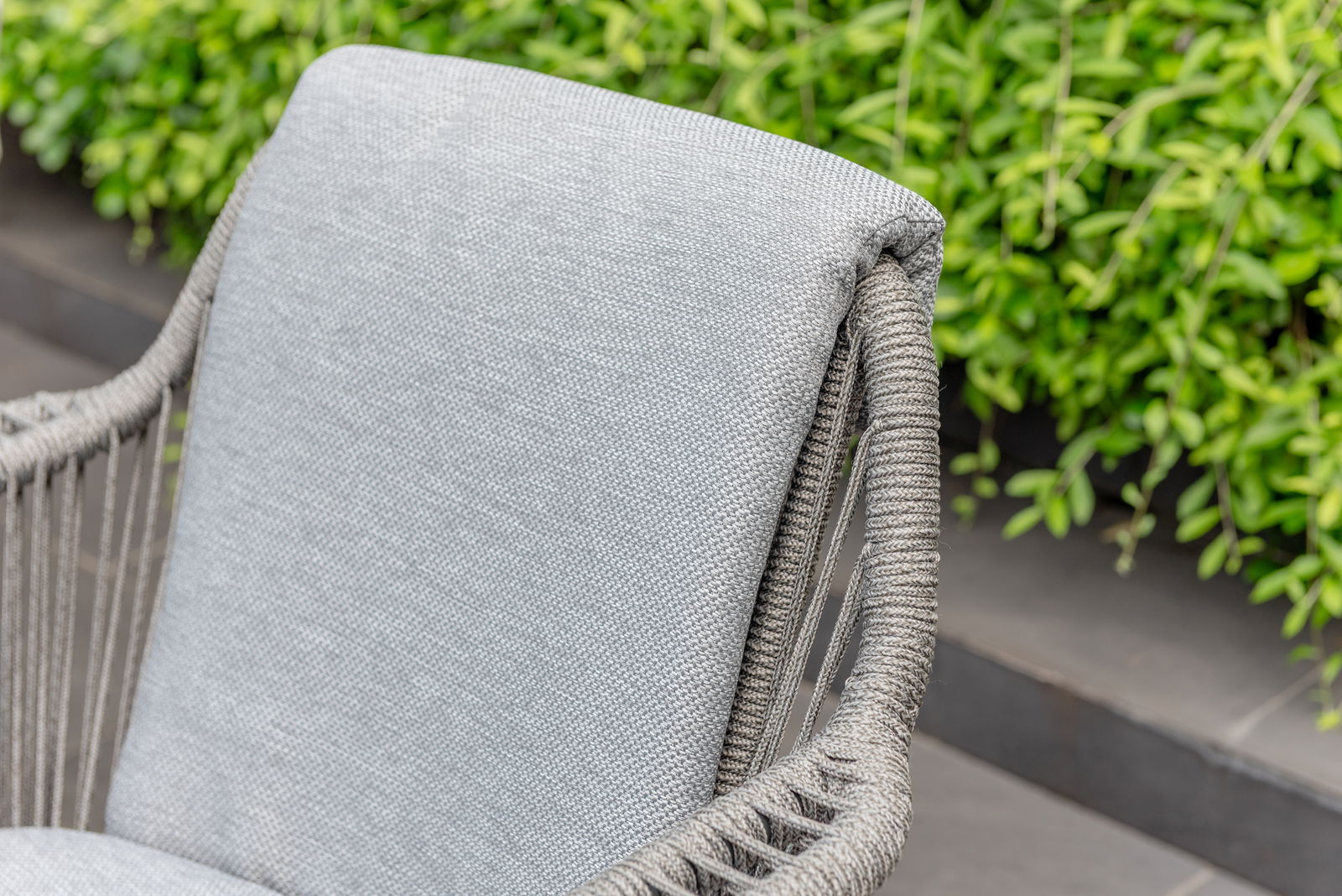 Nahaufnahme eines grauen Armlehnstuhls mit geflochtenem Seilrahmen, seitliche Perspektive