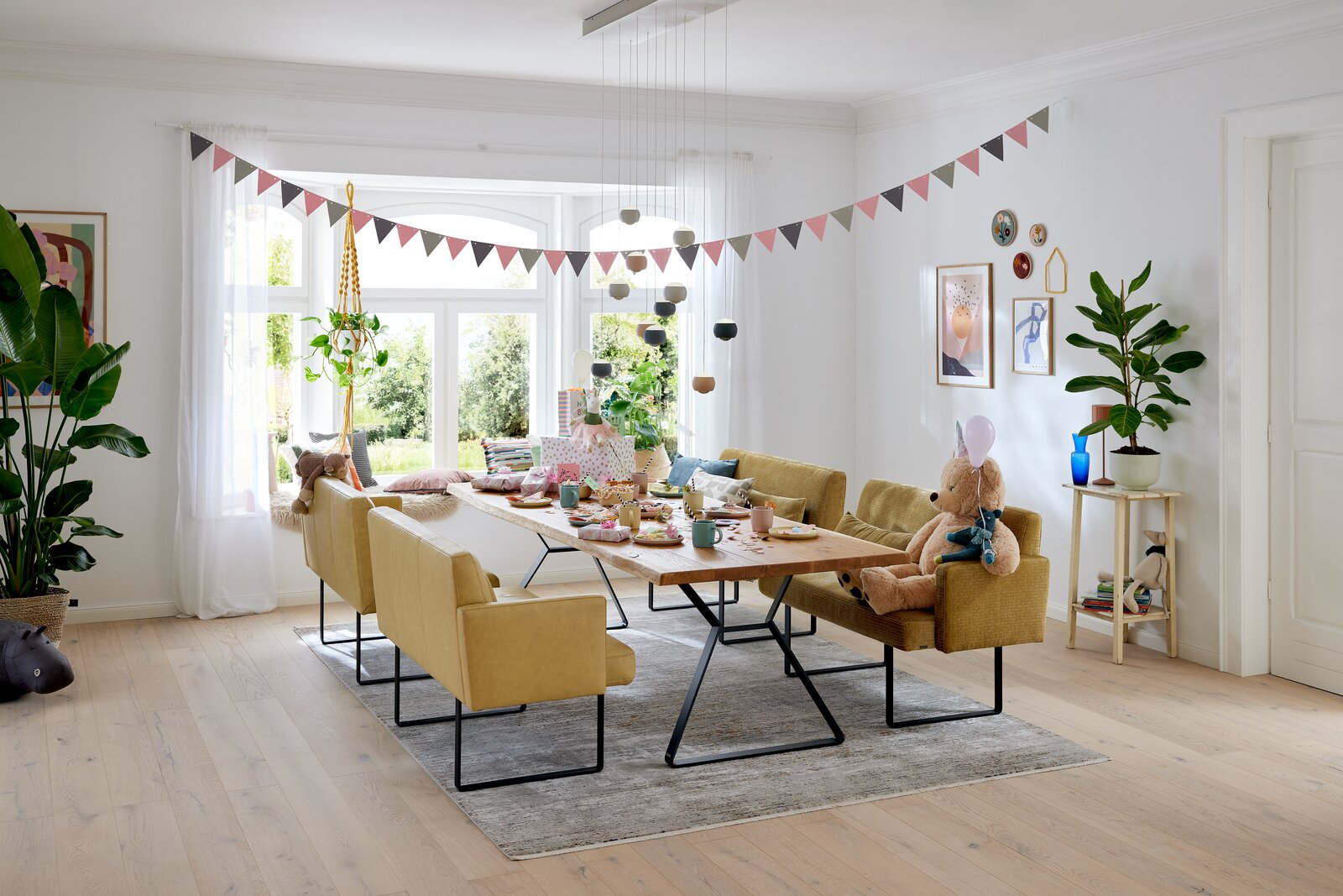 Gemütliche Esszimmer-Szene mit modernen, gelben Bänken und einem Holztisch, dekoriert für eine Feier. Perspektive von der Seite.