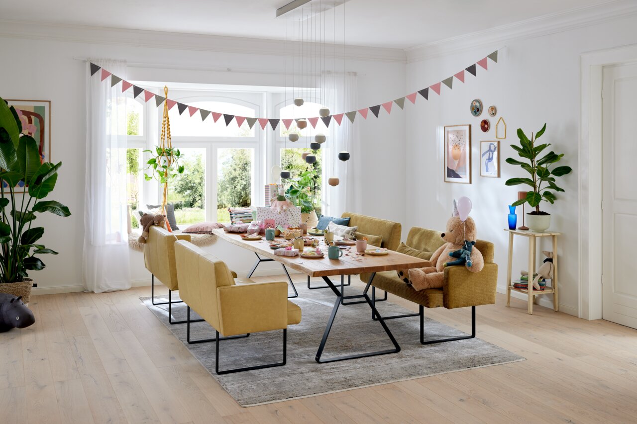 Musterring Bank 1,5 XL MR 4010 Gezellige eetkamer met moderne, gele banken en een houten tafel, versierd voor een feestje. Aanzicht vanaf de zijkant.