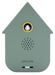 Vorderansicht einer modernen, grünlichen Soundbox in Form eines Hauses mit einem kleinen Vogel in einem runden Fenster und Lautsprecherlöchern darunter.