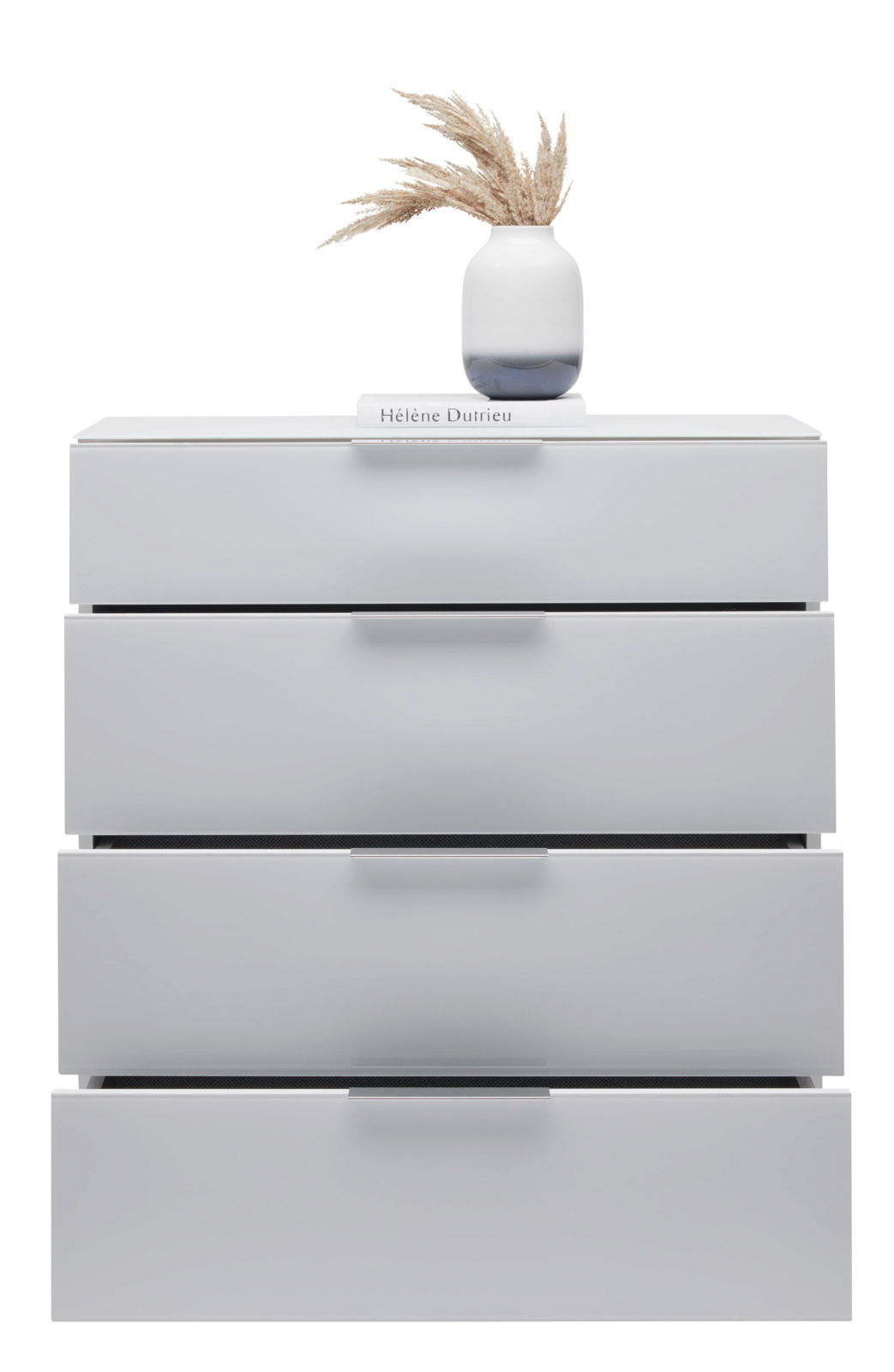 Weiße Schubkastenkommode mit vier Schubladen, darauf eine Vase mit getrockneten Gräsern und ein Buch, frontale Perspektive.