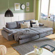 Graues Ecksofa INFERNO mit verstellbaren Rückenlehnen und Kissen, in einem modernen Wohnzimmer mit grüner Wand und großen Fenstern, von vorne betrachtet.