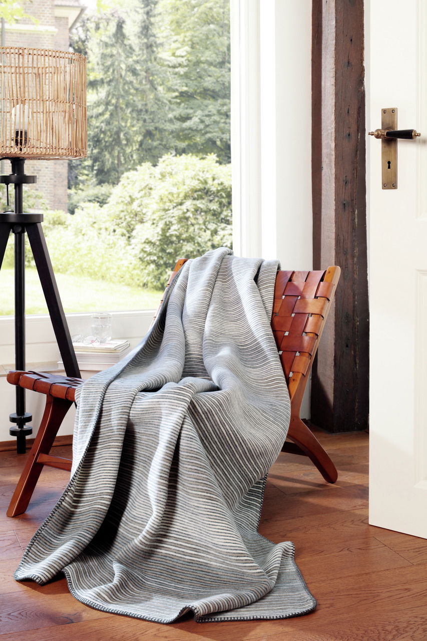 Graue gestreifte Wohndecke auf einem Holzstuhl in einem hellen Raum mit Blick nach draußen.