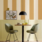 Schwarze, halbrunde Pendelleuchte über einem kleinen Holztisch mit zwei grünen Polsterstühlen vor einer gestreiften Wand und Schmetterlingsbild, Frontansicht auf Augenhöhe.