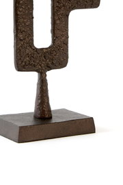 Close-up vanuit licht schuin vooraanzicht van een donkerbruin abstract metalen sculptuur met reliëfstructuur op een rechthoekige sokkel tegen een witte achtergrond.