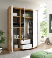 Moderne drievleugelige draaideurkast in houtlook met witte deuren, gedeeltelijk geopend, met daarin vakken met kleding en accessoires. Perspectief: vooraanzicht.