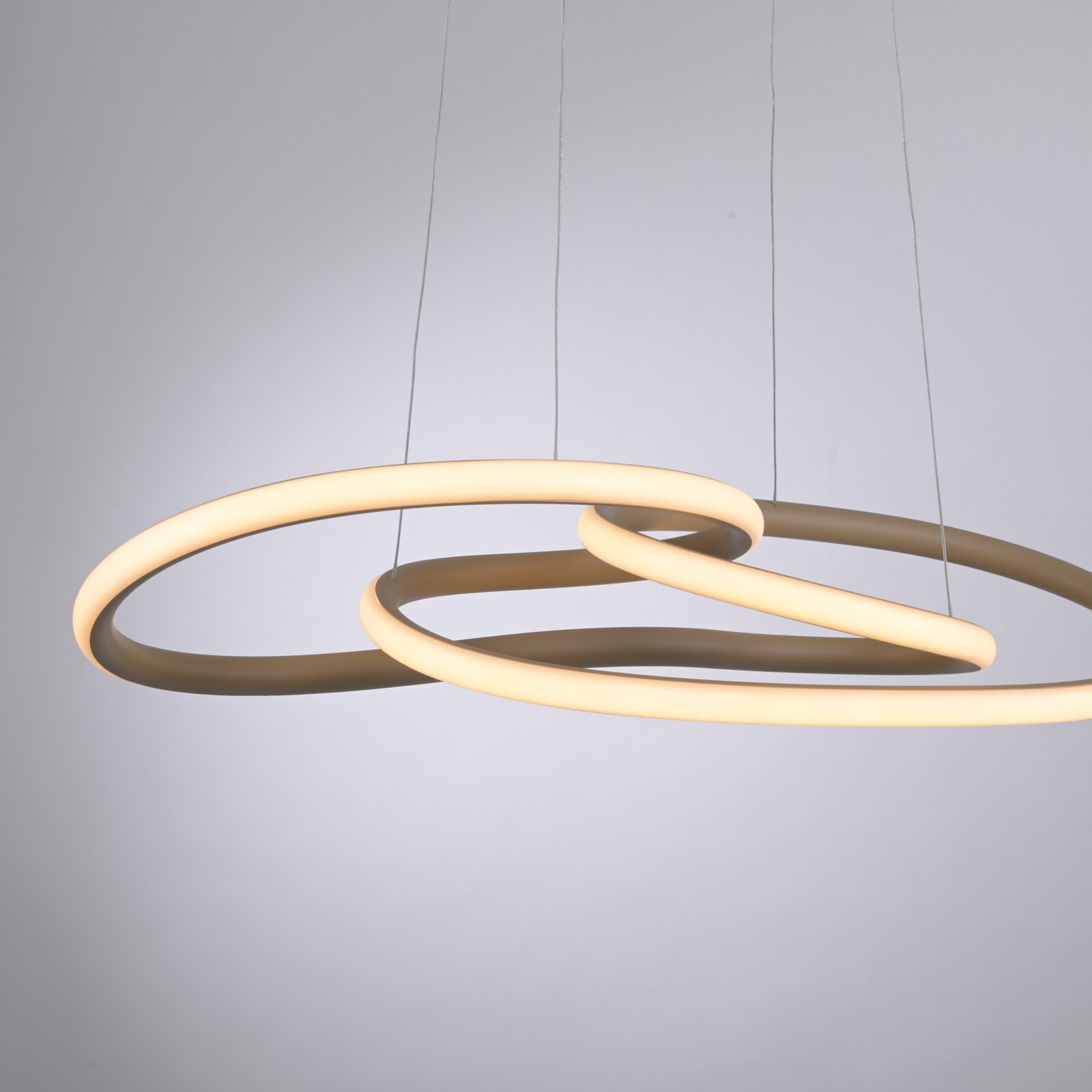 Moderne LED-Pendelleuchte mit zwei überlappenden, ringförmigen Lichtbändern in warmweiß, an dünnen Seilen aufgehängt; Ansicht leicht von unten in Perspektive vor hellem Hintergrund