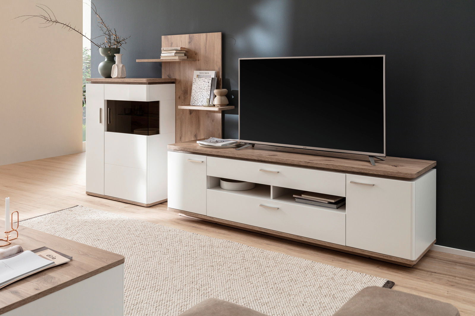 Moderne Wandkombination mit weißem und holzfarbenem Design, bestehend aus einem TV-Schrank und einem hohen Schrank, seitliche Perspektive.