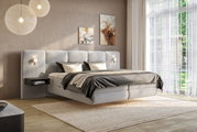 Modernes Boxspringbett in einem stilvollen Schlafzimmer mit weichen grauen Polstern, seitlichen Nachttischen und eleganter Beleuchtung, aus der Perspektive von vorne rechts betrachtet.