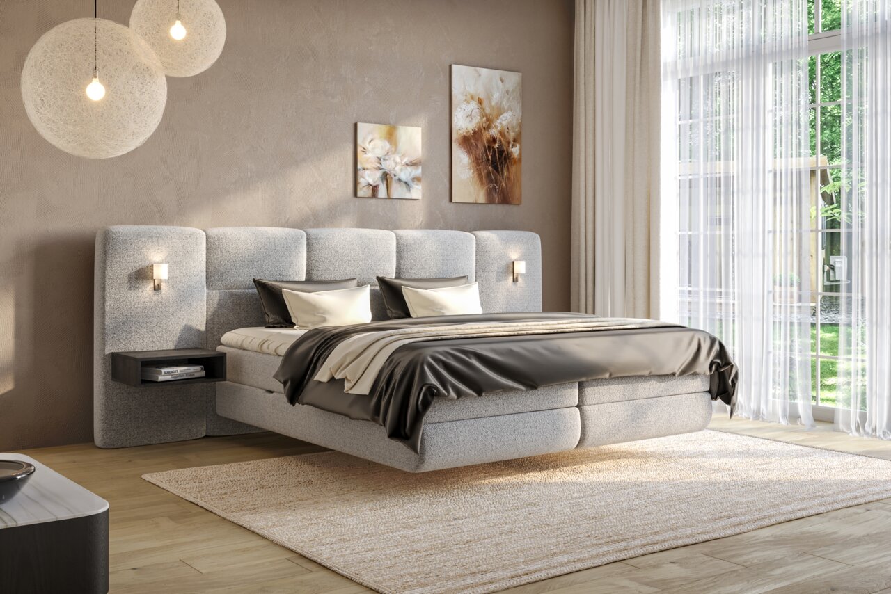 Modernes Boxspringbett in einem stilvollen Schlafzimmer mit weichen grauen Polstern, seitlichen Nachttischen und eleganter Beleuchtung, aus der Perspektive von vorne rechts betrachtet.