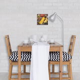 Glasbild mit Pasta-Motiven, an einer weißen Ziegelwand über einem Esstisch mit Holzstühlen und schwarz-weiß gemusterten Kissen aufgehängt, aus der Perspektive eines Betrachters im Raum.