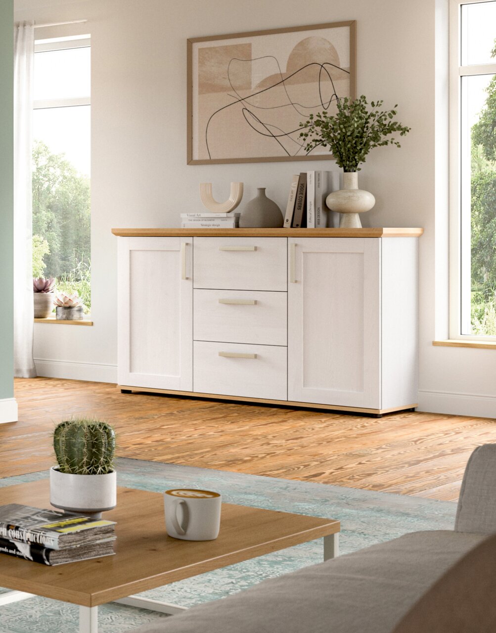 Weißes Sideboard mit Holzoberfläche, drei Schubladen und zwei Türen, dekoriert mit Vasen und Büchern, in einem hellen Wohnzimmer mit Holzboden, seitliche Perspektive.