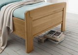 Komfortbett aus Holz mit hellblauer Bettwäsche und beiger Decke, seitliche Perspektive