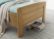 Comfortabel houten bed met lichtblauw beddengoed en een beige deken, zijaanzicht