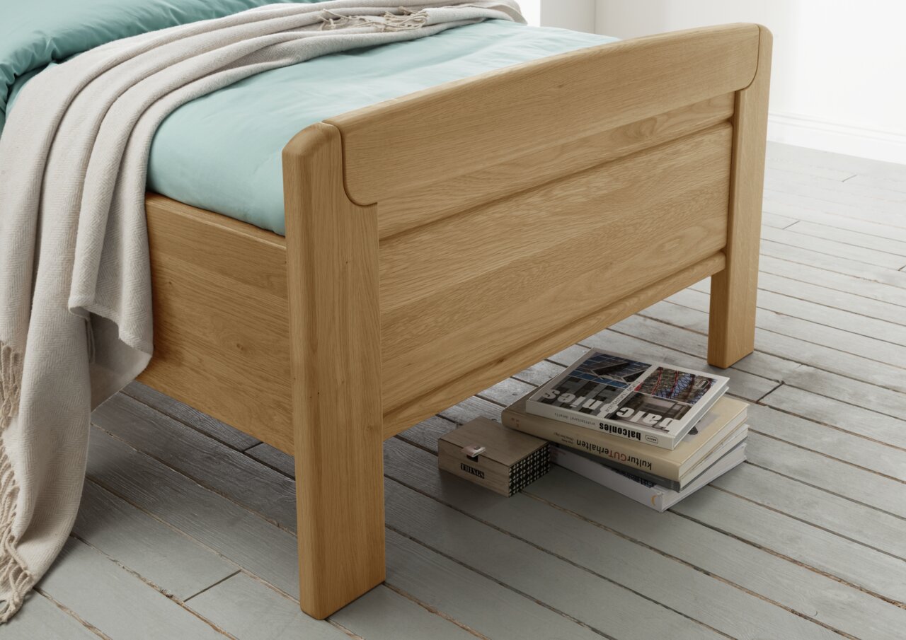 Comfortabel houten bed met lichtblauw beddengoed en een beige deken, zijaanzicht