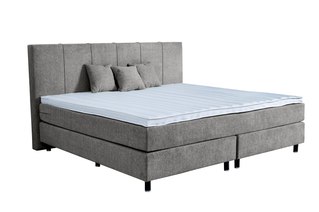 Graues Boxspringbett mit hohem Kopfteil und drei Kissen, seitliche Perspektive