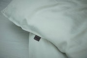 Nahaufnahme einer hellgrauen Bettwäsche mit sichtbarem Etikett, Perspektive von oben.