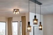 Moderne Pendelleuchte mit drei zylindrischen, geriffelten Glasschirmen und warmem Licht über einem Wohnbereich, fotografiert aus leicht schräger Untersicht (Blick nach oben)