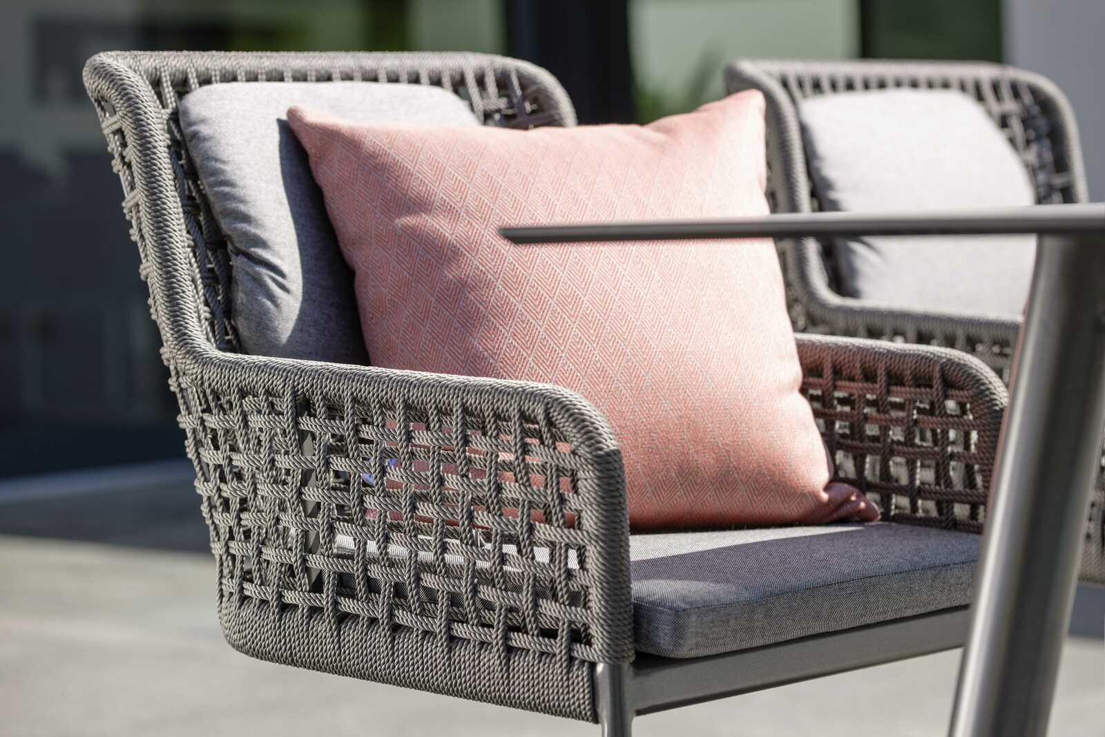 Nahaufnahme eines modernen Freischwingersessels mit grauem Geflecht und einem rosa Kissen, seitliche Perspektive.