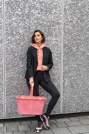 Frau in sportlicher Kleidung lehnt an einer Wand und hält einen pinken Einkaufskorb in der Hand, seitliche Perspektive