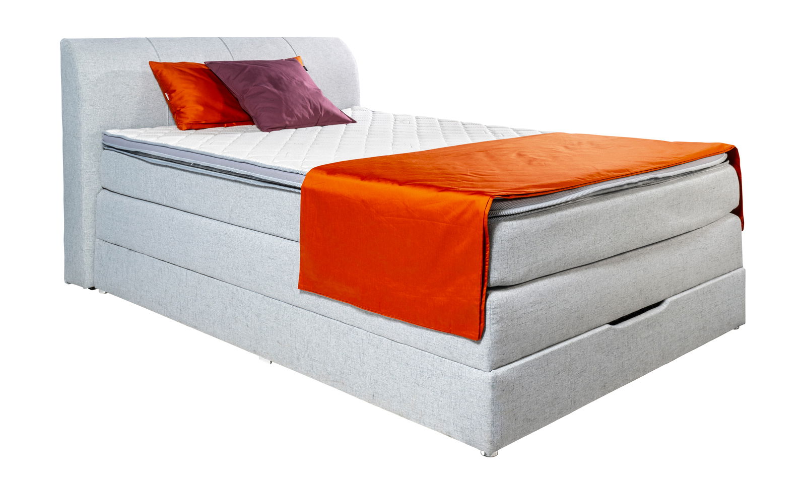 Boxspringbett in seitlicher Perspektive mit grauem Stoffbezug, zwei Kissen in Orange und Lila sowie einer orangefarbenen Decke.