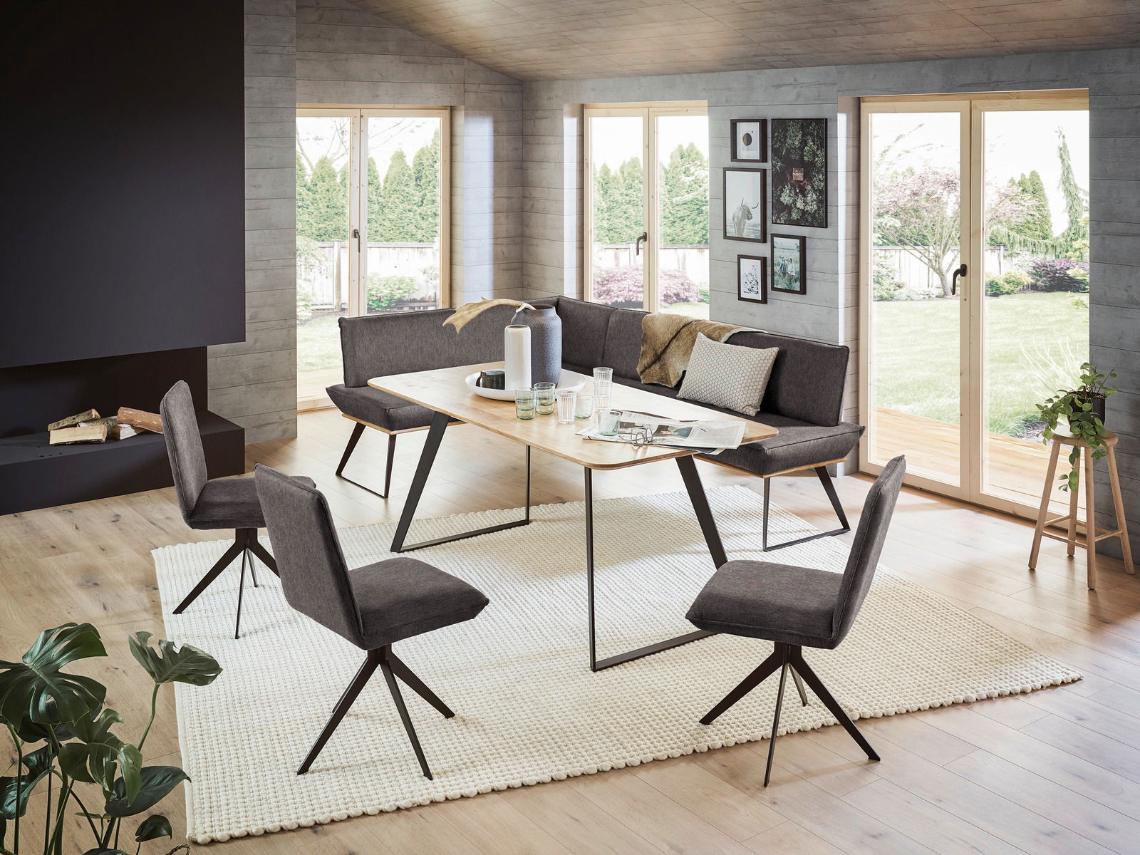 Voleo Hoekbank MALIBU Moderne Esszimmer-Eckbank mit Esstisch und Stühlen in einem hellen Raum mit großen Fenstern, seitliche Perspektive.