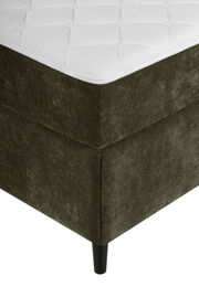 Ecke eines Boxbetts mit dunkelgrünem Stoffbezug und schwarzem Bein, aus der Perspektive von unten links.