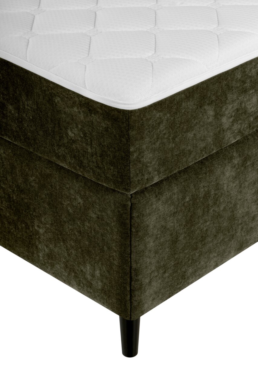 Ecke eines Boxbetts mit dunkelgrünem Stoffbezug und schwarzem Bein, aus der Perspektive von unten links.