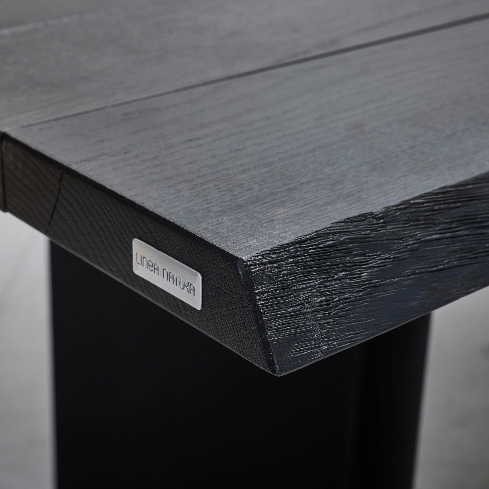 Nahaufnahme der Tischkante eines Esstisches mit natürlicher Holzstruktur und Metallplakette, Perspektive von der Seite