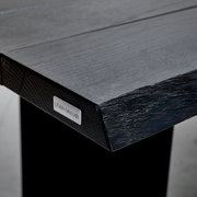 Nahaufnahme der Tischkante eines Esstisches mit natürlicher Holzstruktur und Metallplakette, Perspektive von der Seite