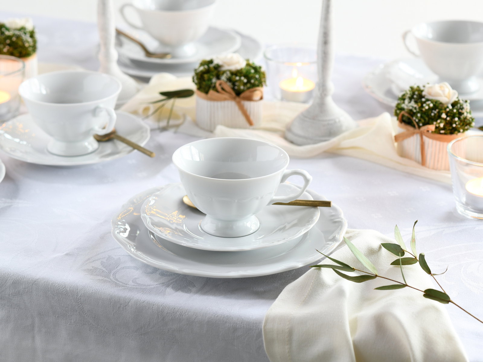 Elegantes weißes Kaffeeservice auf einem gedeckten Tisch mit Kerzen und Dekorationen, seitliche Perspektive