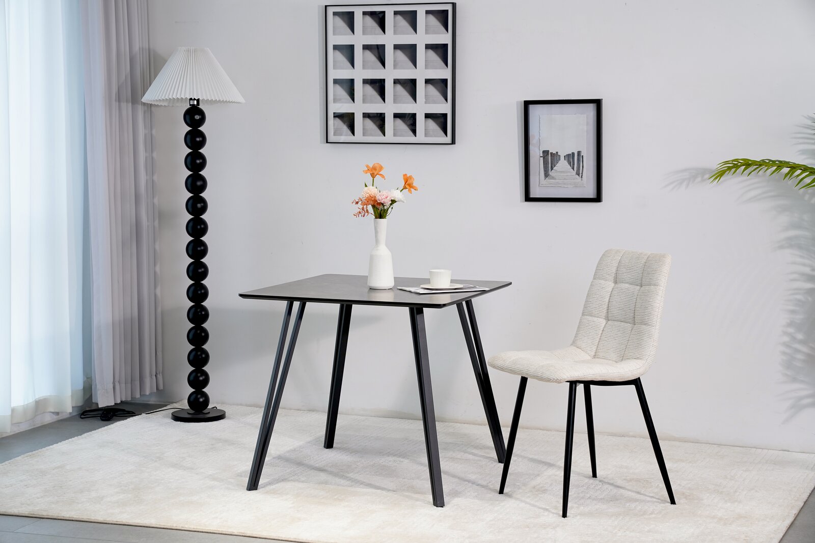 Moderner Esstisch mit schwarzer Tischplatte und schrägen Beinen, seitliche Perspektive, dekoriert mit einer Vase und Blumen.