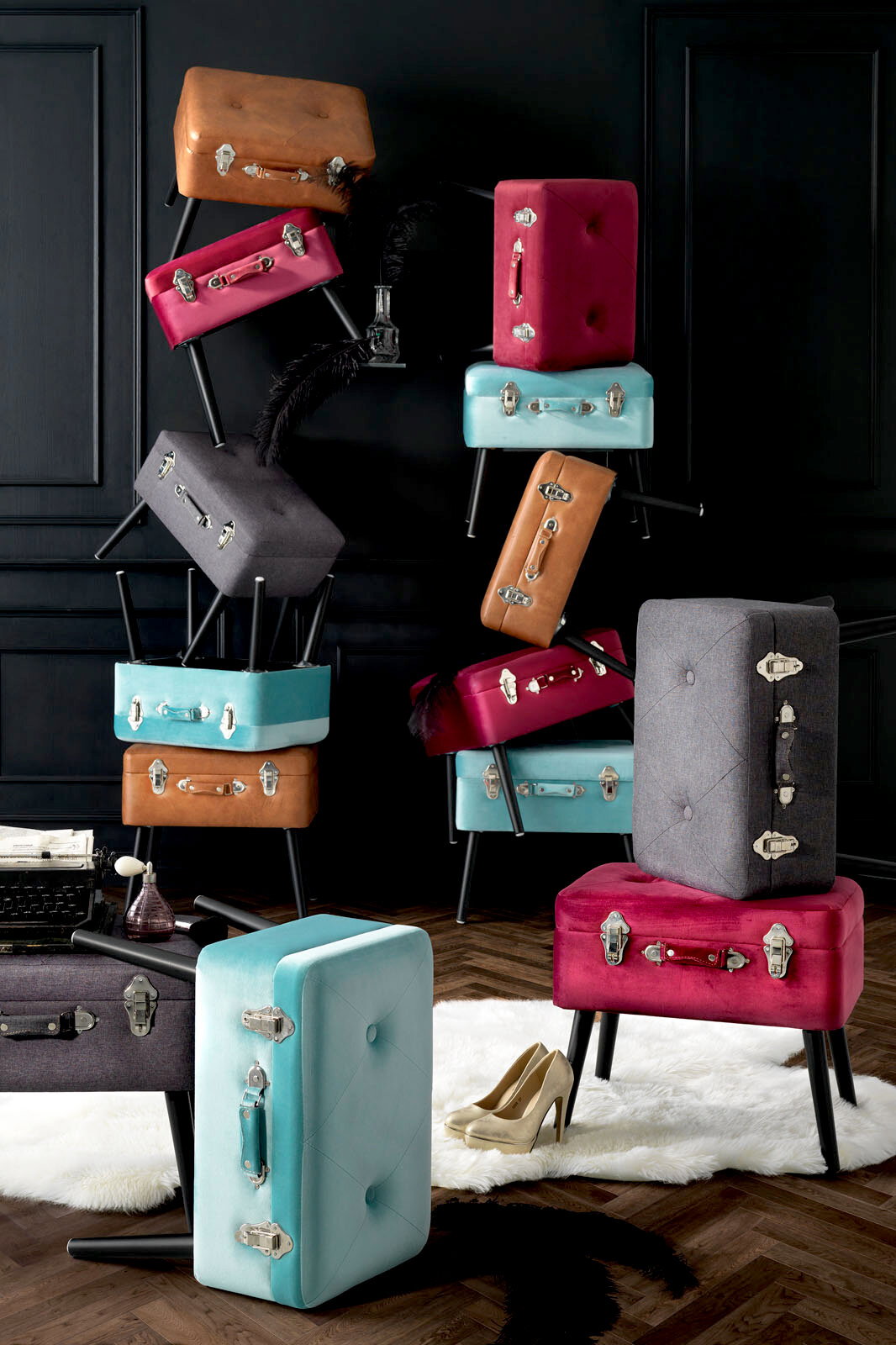 Stilvolle Kofferhocker in verschiedenen Farben, gestapelt in einem eleganten Raum mit dunkler Wandverkleidung, aus seitlicher Perspektive.