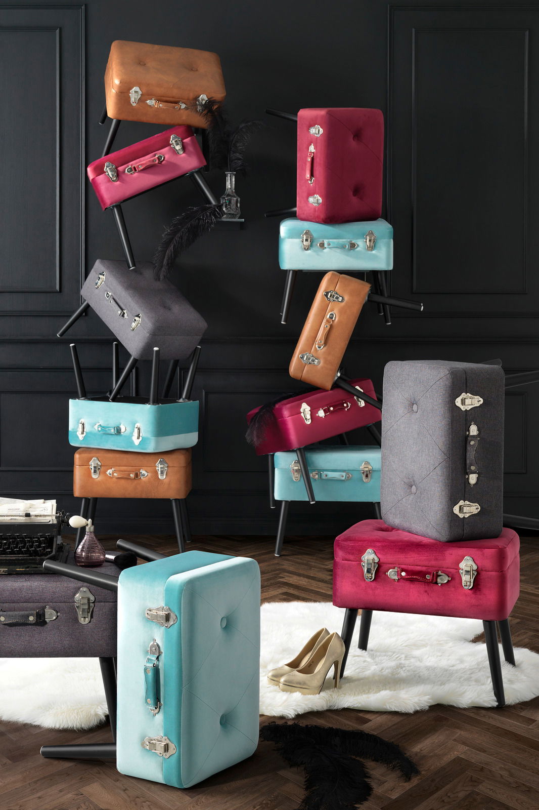 Stilvolle Kofferhocker in verschiedenen Farben, gestapelt in einem eleganten Raum mit dunkler Wandverkleidung, aus seitlicher Perspektive.