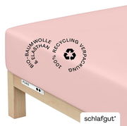 Rosa Spannbettlaken aus Bio-Baumwolle und Elasthan, auf einer Matratze gespannt, mit Hinweis auf 100% recycelte Verpackung, seitliche Perspektive.