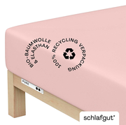 Rosa Spannbettlaken aus Bio-Baumwolle und Elasthan, auf einer Matratze gespannt, mit Hinweis auf 100% recycelte Verpackung, seitliche Perspektive.