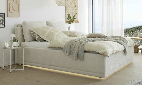 Modernes Polsterbettgestell in einem hellen Raum, seitliche Perspektive mit stilvoller Bettwäsche und Nachttisch.