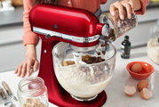 Rote Küchenmaschine Liebesapfel in der Seitenansicht, während Schokoladenstückchen in die Rührschüssel gegeben werden.