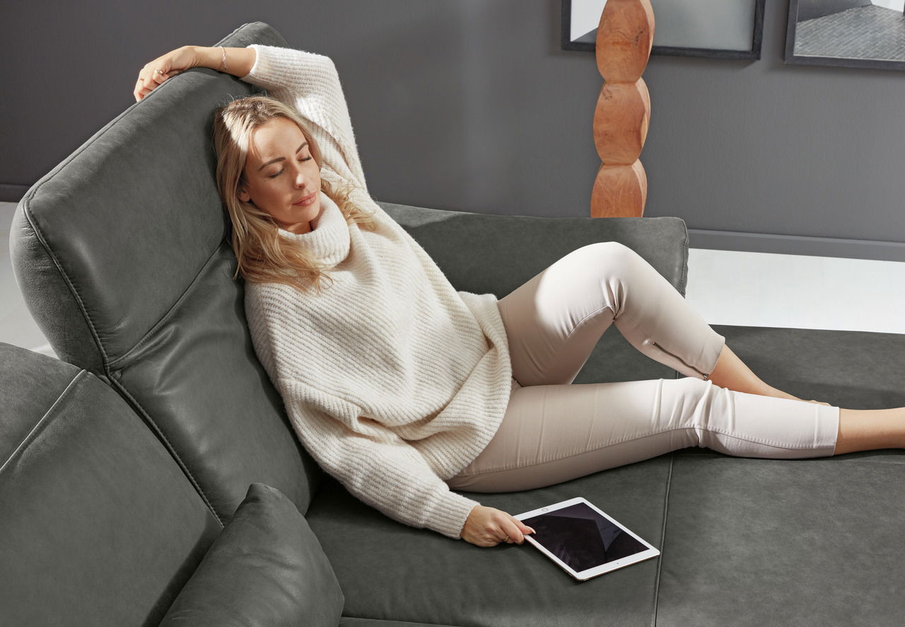 Frau entspannt auf einer grauen Longchairkombination, seitliche Perspektive