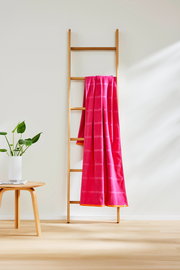 Ein pinkfarbenes Strandtuch mit Karomuster hängt über einer Holzleiter, seitliche Perspektive.